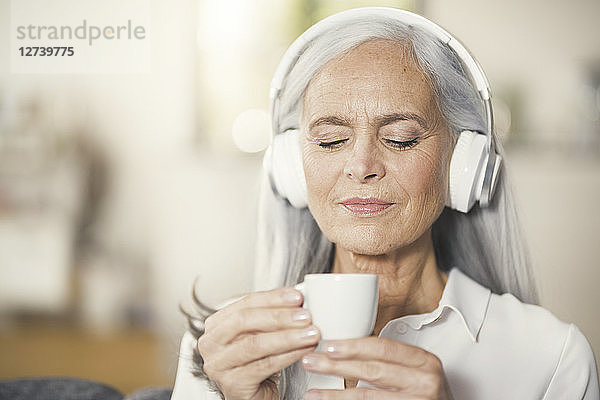Senior woman listen music with headphones and drinking coffee