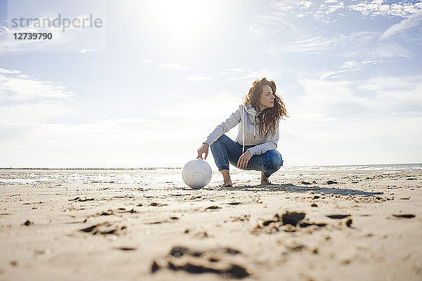 Woman with soccer ball crouching on the beach  looking away