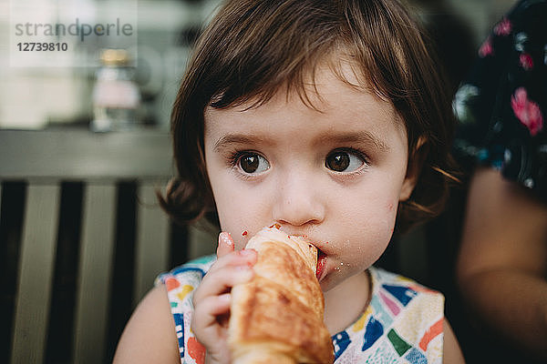 Portrait of baby girl eating a croissant