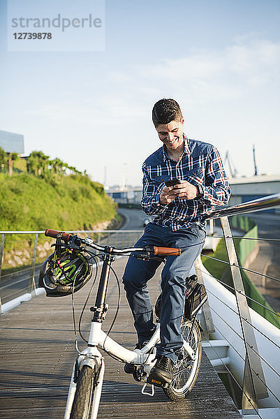 Smiling young man with bicycle looking at smartphone