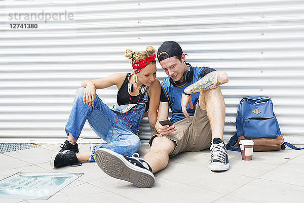 Young couple sitting on ground looking at smartphone