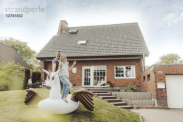 Happy mature couple with inflatable pool toy in garden of their home