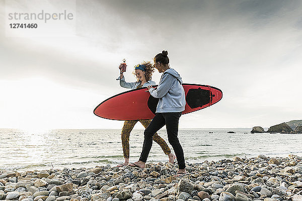 Happy friends with surfboard walking on stony beach