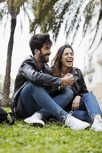 Spain  Barcelona  laughing young couple sitting on meadow