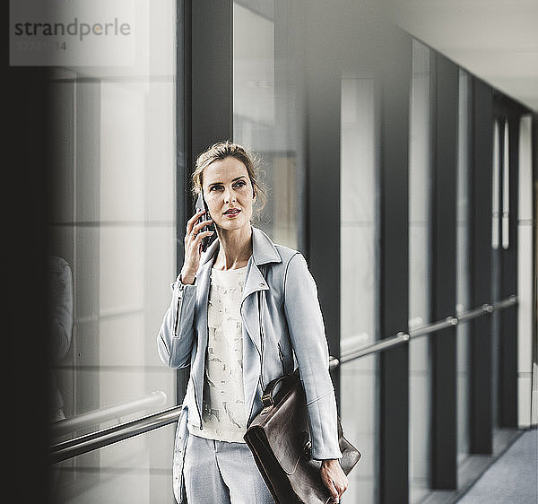 Businesswoman on cell phone at the window in office passageway