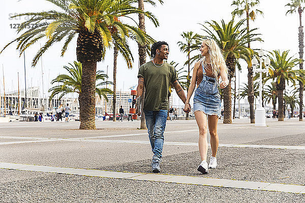 Spain  Barcelona  multicultural young couple walking hand in hand on promenade