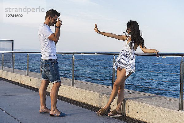 Young urban couple taking pictures by the sea  woman making peace sign