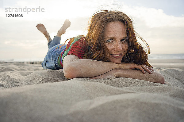 Redheaded woman lying in sand on the beach  smiling
