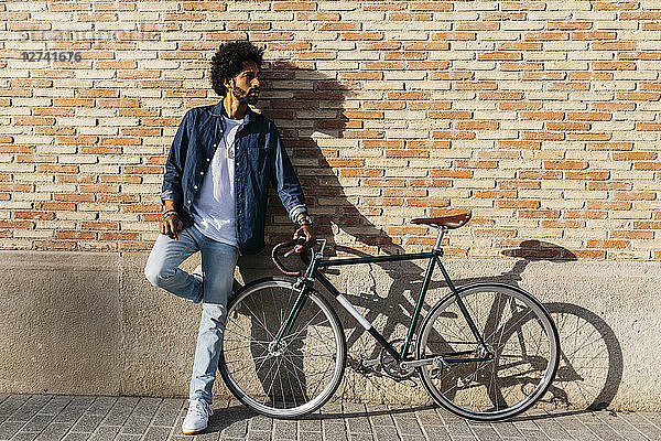 Young man with racing cycle leaning against brick wall
