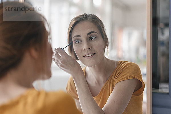 Woman applying mascara in front of mirror