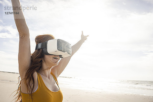 Redheaded woman using VR glasses on the beach