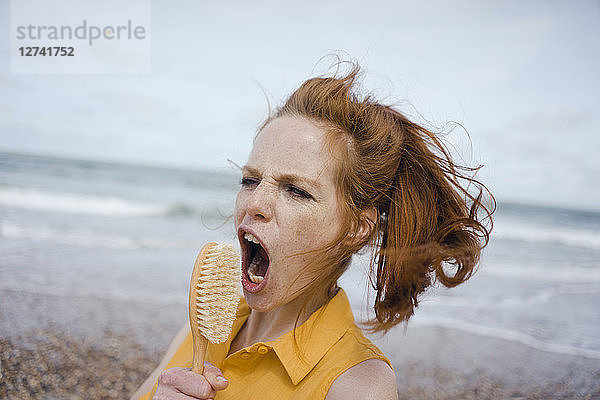 Woman using hair brush at the sea as a microphone