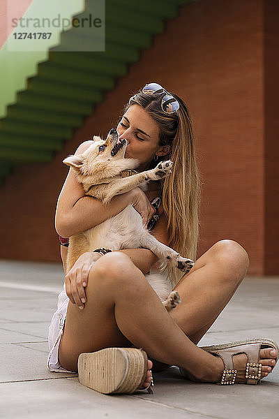 Smiling young woman sitting and kissing her dog