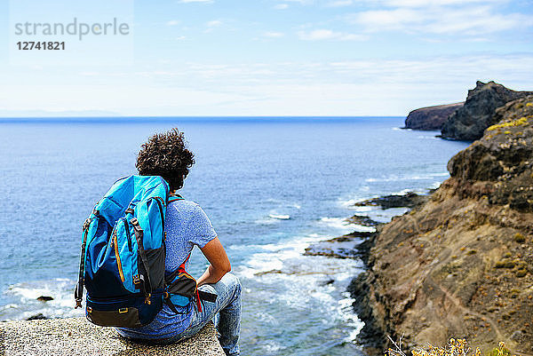 Spain  Canary Islands  Gran Canaria  Man with backpack sitting on cliff