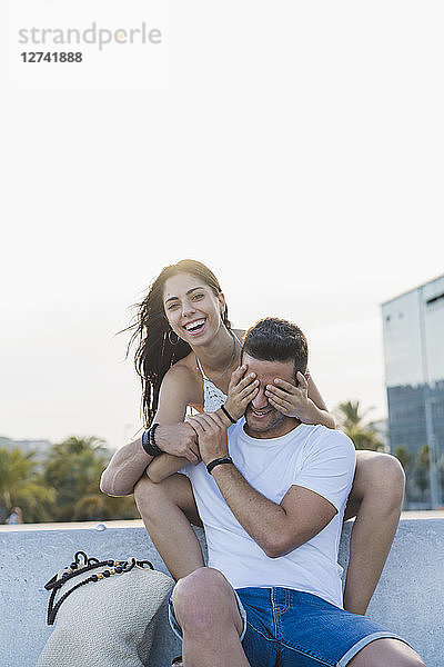 Laughing young woman surprising her boyfriend  covering his eyes