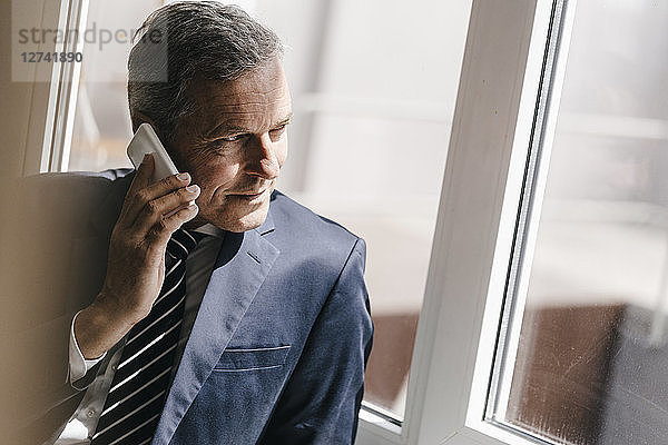Smiling mature businessman on cell phone looking out of window