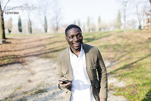 Portrait ogf young man in park  wearing jacket  holding smartphone