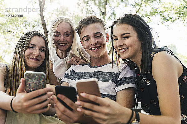 Group of smiling friends looking at cell phones outdoors