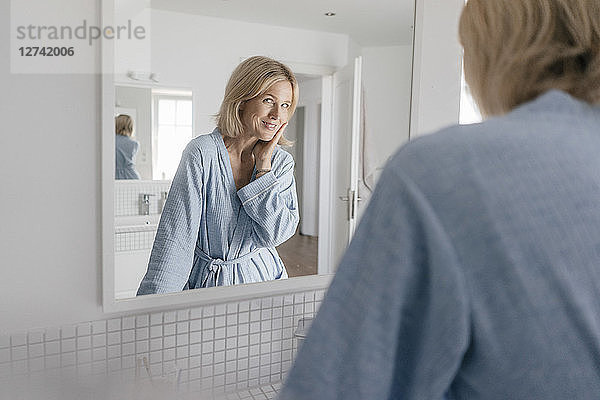 Portrait of smiling mature woman looking in bathroom mirror