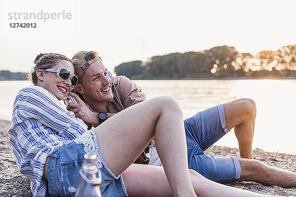 Young couple relaxing at the riverbank sharing headphones