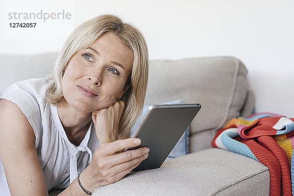 Portrait of mature woman lying on couch at home holding tablet