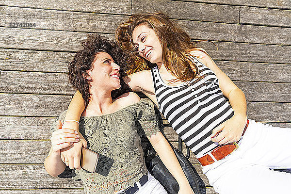 Two happy female friends lying down on a wooden floor