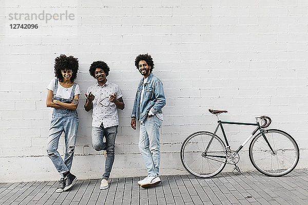 Group of three friends with racing cycle leaning against wall