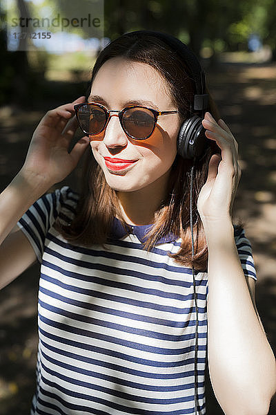 Portrait of smiling young woman wearing sunglasses listening music with headphones