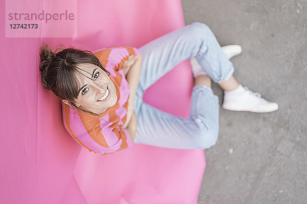 Confident young woman sitting on pink background