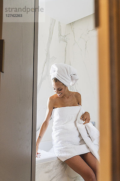 Woman wrapped in towels  sitting on edge of bathtub