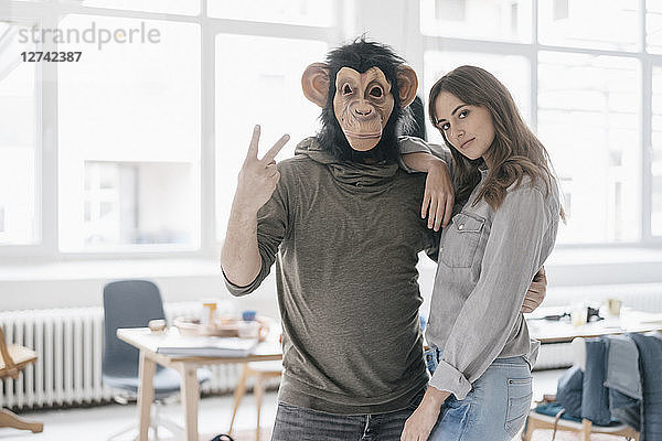 Man wearing chimpanzee mask  making victory-sign  woman leaning on him