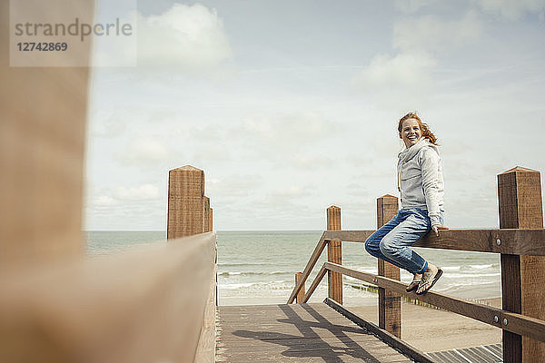 Woman sitting on fence at the sea  smiling