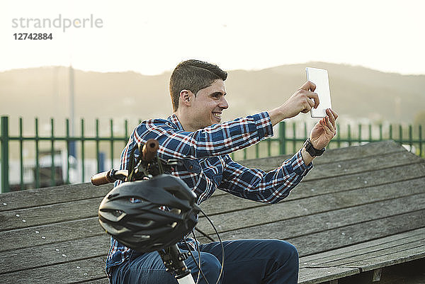 Smiling young man with bicycle taking a selfie with a tablet
