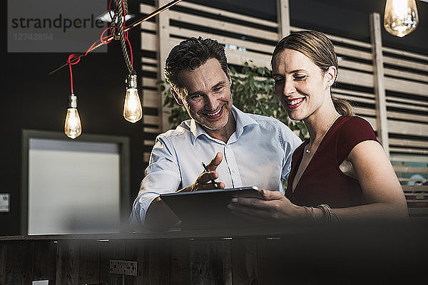 Smiling businesswoman and businessman with tablet discussing in office