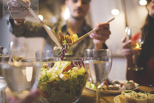 Man serving salad at dinner with family and friends