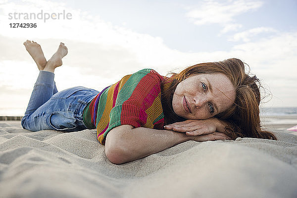 Redheaded woman lying in sand on the beach