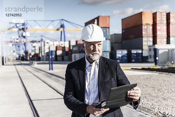 Businessman at cargo harbour  wearing safety helmet  using smartphone
