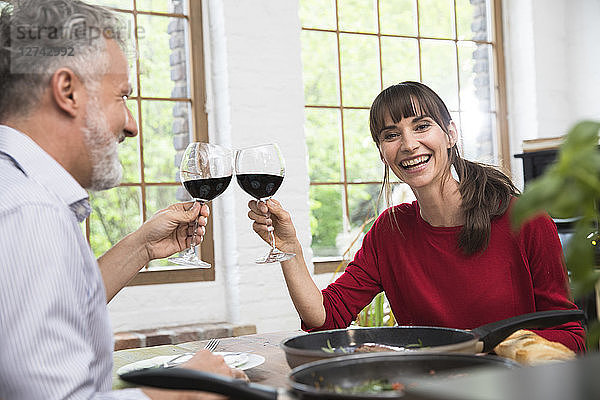 Happy couple sitting in kitchen  toasting with red wine  enjoying dinner