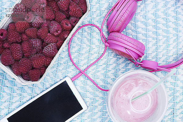 Box of raspberries  smoothie  smartphone and pink headphones on blanket