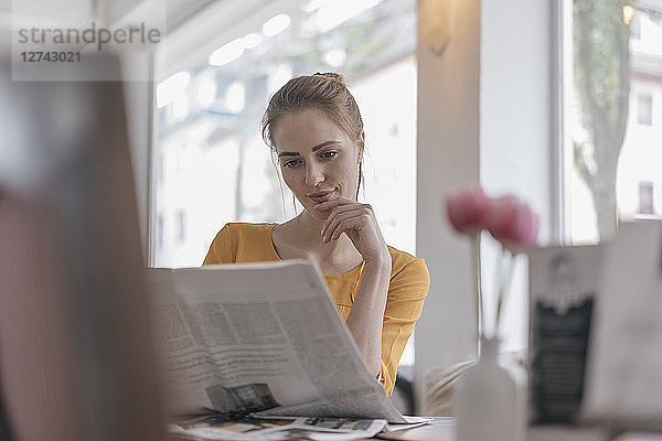 Young woman sitting in coworking space  reading newspaper