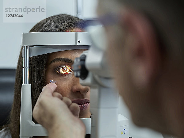 Optometrist examining young woman's eye  contact lens on index finger