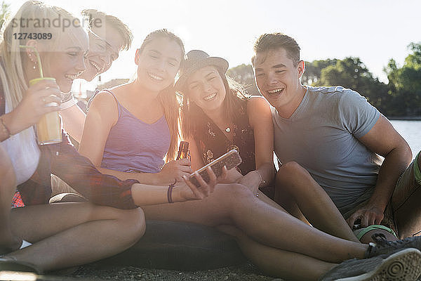 Group of happy friends sitting outdoors with drinks and cell phone