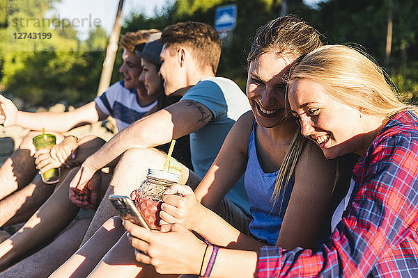 Group of happy friends sitting outdoors with refreshing drinks and cell phones