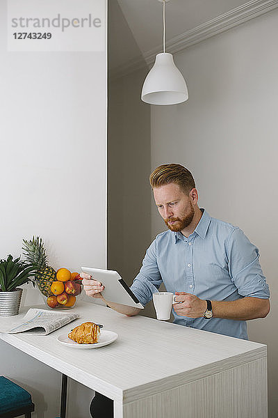 Businessman drinking coffee while using tablet at home