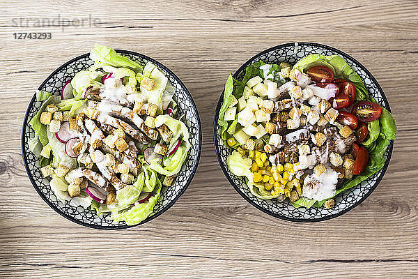Two bowls of various Caesar salads with meat