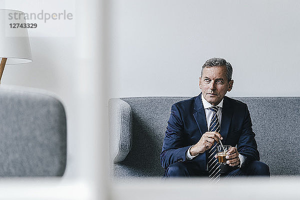 Mature businessman with glass of coffee sitting on couch in his office