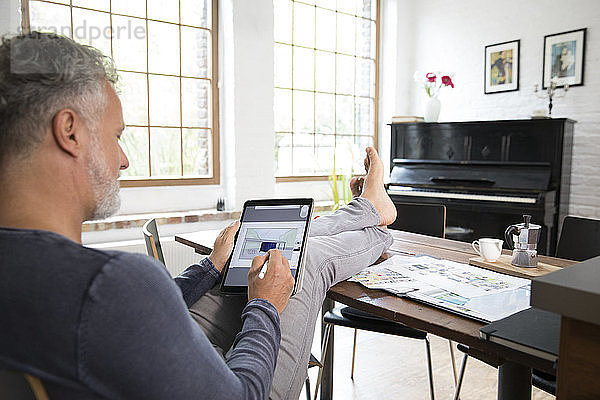 Mature man working from his home office with feet up  using tablet