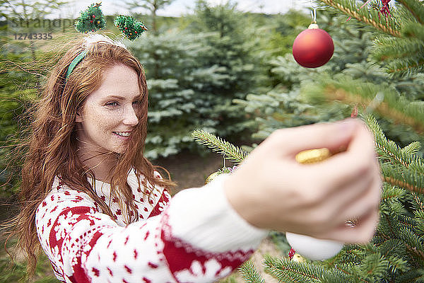 Redheaded young woman decorating Christmas tree outdoors