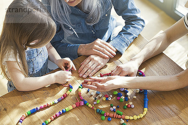 Grandmother and granddaughter and mother threading beads