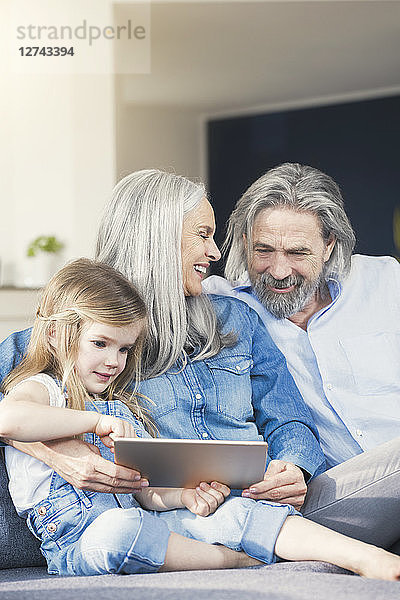 Grandparents and granddaughter sitting on couch  using tablet